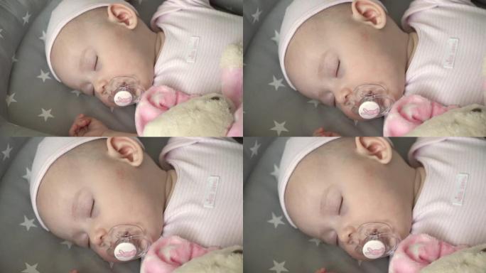 戴着帽子的新生小女孩的特写镜头，用奶嘴睡在摇篮里的粉色泰迪熊附近。爱和儿童保育的概念。