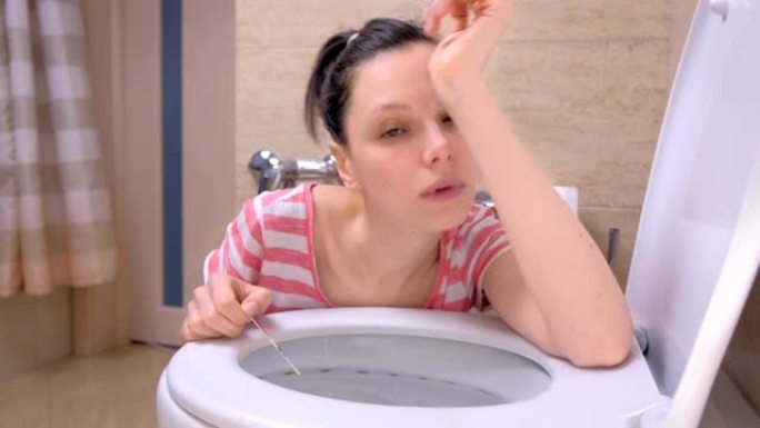 孕妇疲倦的女人坐在家里的地板上看着相机在厕所里呕吐。