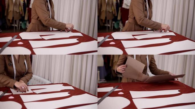 专业女裁缝在工作室里用红布在餐桌旁工作。熟练的女裁缝正在使用图案用肥皂或粉笔在红色织物上绘制素描线。