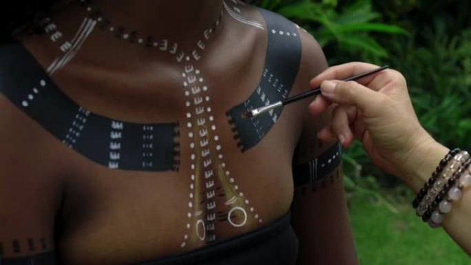 坐在热带花园里的非洲女孩化妆并在身体上画了民族线条