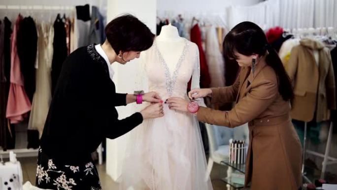 两位女设计师的肖像通过独家订购缝制面料并在人体模型上固定细节来制作婚纱。婚纱的生产。小生意