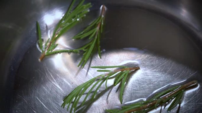 将新鲜的迷迭香树枝倒入不锈钢锅中的热油中的高角度