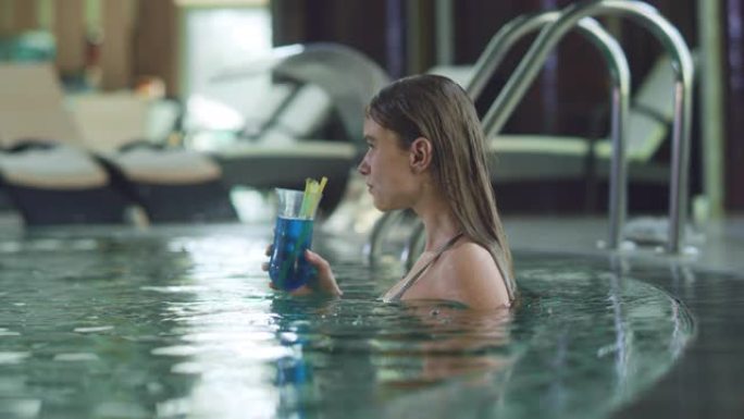 性感的女人在豪华游泳池享受鸡尾酒。女人啜饮酒精