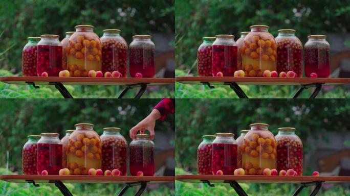 在花园的桌子上关闭罐装果汁和水果和浆果。无法辨认的女人拿走了密封的蜜饯罐