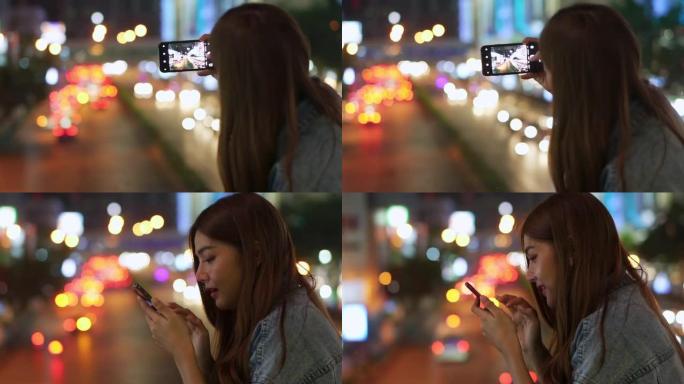 年轻美丽的亚洲女孩晚上在城市里散步享受使用智能手机相机与移动应用程序拍摄照片或记录照明城市景观的视频