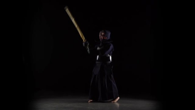 强壮的剑道大师在黑色背景上练习武术