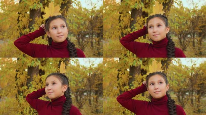 黑发女孩，辫子像秋天公园的女王一样，头后拿着枫叶。秋天公园的肖像女孩少年头顶着黄叶像皇冠。