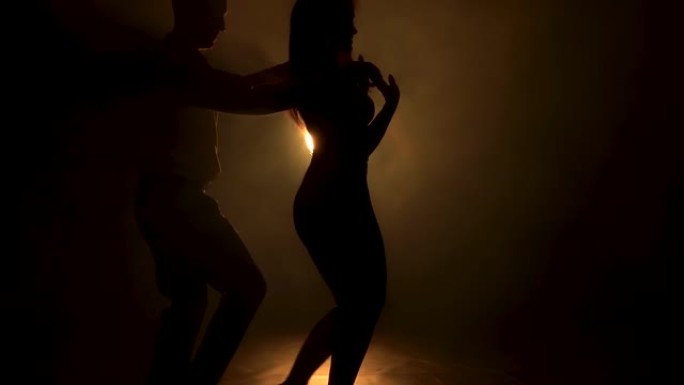 两个性感的拉丁舞者的肖像在一个黑烟的工作室里跳着性感的舞蹈，黄色的灯光。年轻夫妇慢动作跳舞萨尔萨舞。