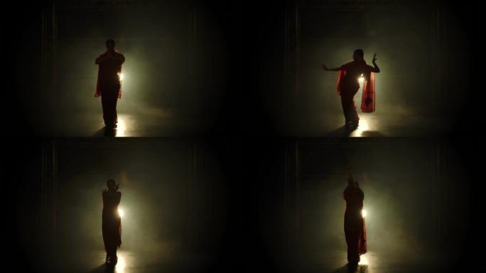剪影一个穿着红色纱丽的年轻女孩舞者。印度民间舞蹈。在黑暗的工作室里拍摄，有烟雾和霓虹灯。慢动作