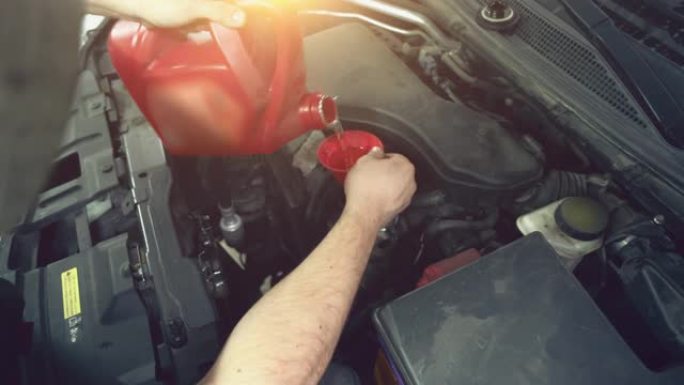 工人在汽车维修时将新的机油从碳罐倒入发动机的漏斗中