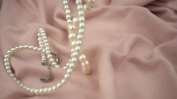 淡粉色柔软织物上的珍珠首饰慢动作。