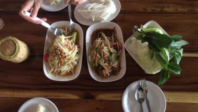 泰国菜餐桌的俯视图拍摄: 吃东北食物 (SOM TUM-辛辣木瓜沙拉，糯米饭，木桌上的烤猪肉沙拉。本