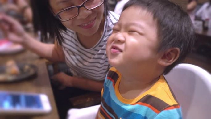 亚洲母亲在一家日本餐厅为儿子用筷子喂食食物
