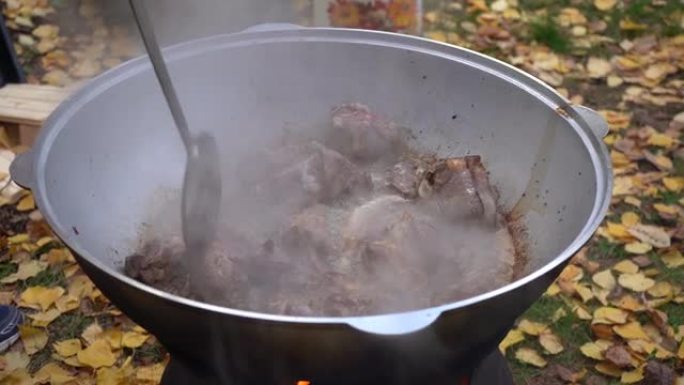 把棕色的肉扔进一个大平底锅里。户外抓饭烹饪肉的特写