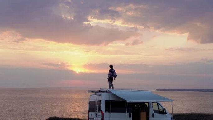 日落时，女人在海边露营车的屋顶上跳舞