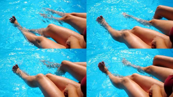 年轻妇女坐在游泳池边，在水中晃来晃去。两个女孩，双腿晒黑，在盆子附近放松。女士们在度假胜地享受假期。