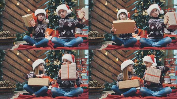 小双胞胎坐在圣诞树下，摇晃着摆弄着礼物的盒子，找出里面的东西。