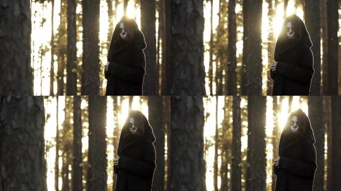 穿着黑色地幔的女巫站在秋天森林的阳光中