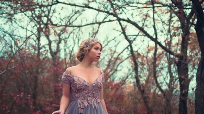 美丽的年轻金发公主站在紫色郁郁葱葱的连衣裙。中世纪迷人女王的复古时尚。皇冠上迷人的女皇。秋园背景，黑