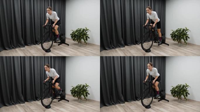 作为比赛准备的一部分，在家里骑固定的自行车教练女子从马鞍上踩踏板，在室内骑自行车。职业自行车