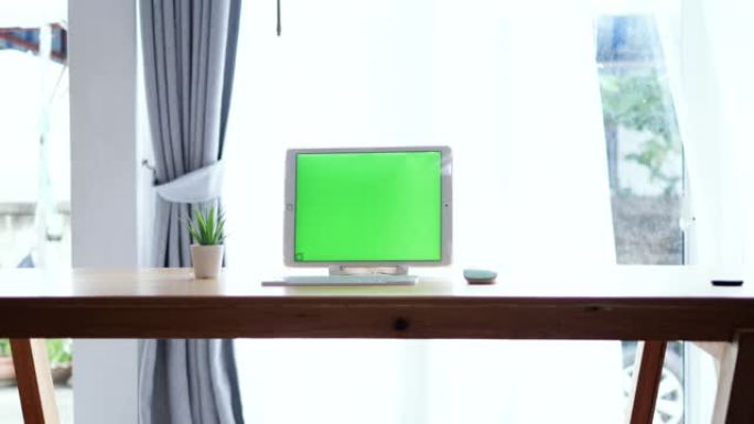 绿色屏幕数字平板电脑放在桌子上，家里有键盘和鼠标，工作工具概念。