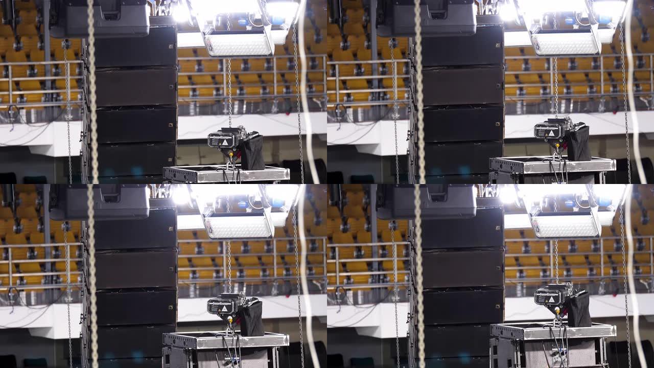 在专业舞台的安装过程中，聚光灯照明设备被提升到桁架上。库存镜头。背景为黄色排座位的音乐会的灯光设备