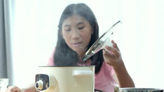 快乐的亚洲孩子在家里做饭时打开火锅。