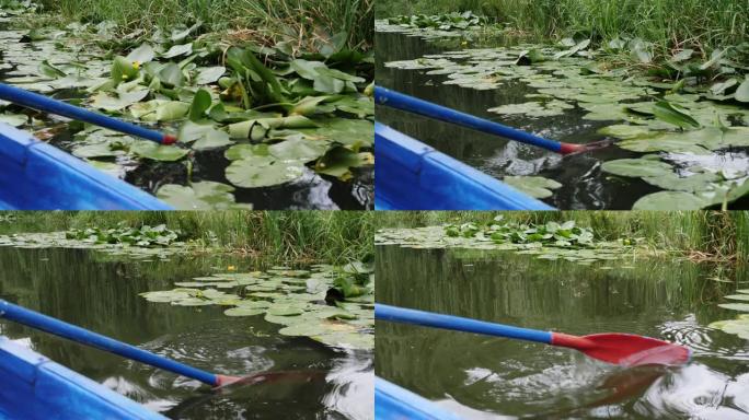 蓝色木制桨在水上。在城市公园的湖面上划桨。在湖上划着睡莲和莎草。在水中划桨的一部分的特写视图。