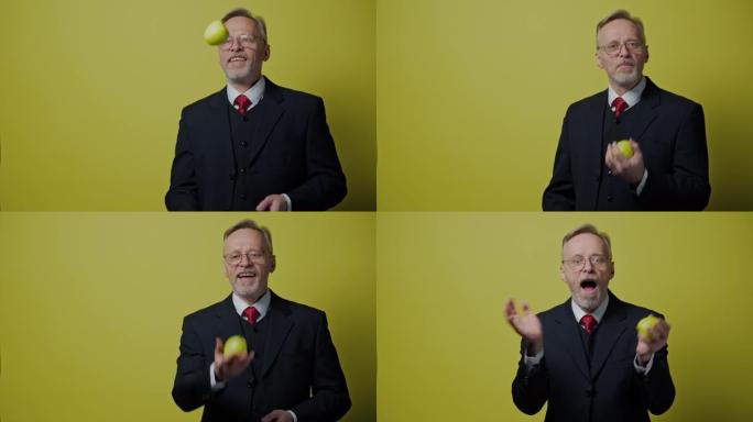 苹果快乐成熟男人的肖像。穿着服装的微笑老商人在黄色背景上玩青苹果。