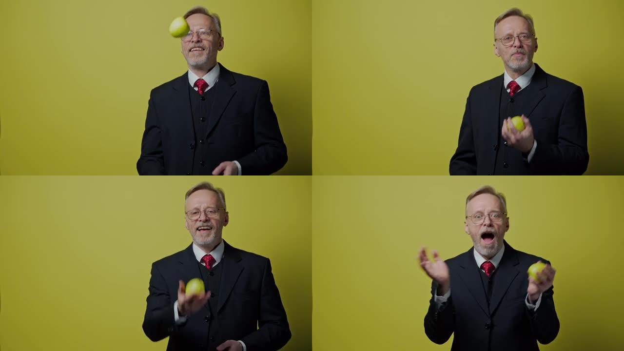 苹果快乐成熟男人的肖像。穿着服装的微笑老商人在黄色背景上玩青苹果。