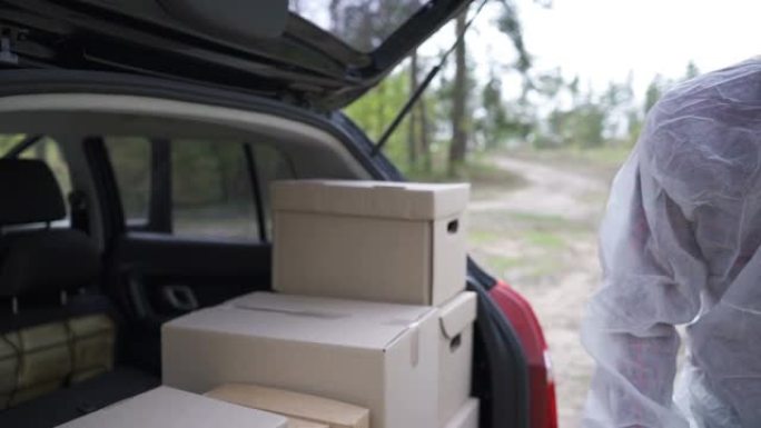一名穿着防护服的志愿者将箱子装入汽车后备箱。冠状病毒大流行期间为家庭工作和社会距离提供送餐服务。网上