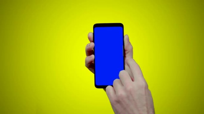 男子手持智能手机，黄色背景上有蓝色croma键，向左侧滑动两次