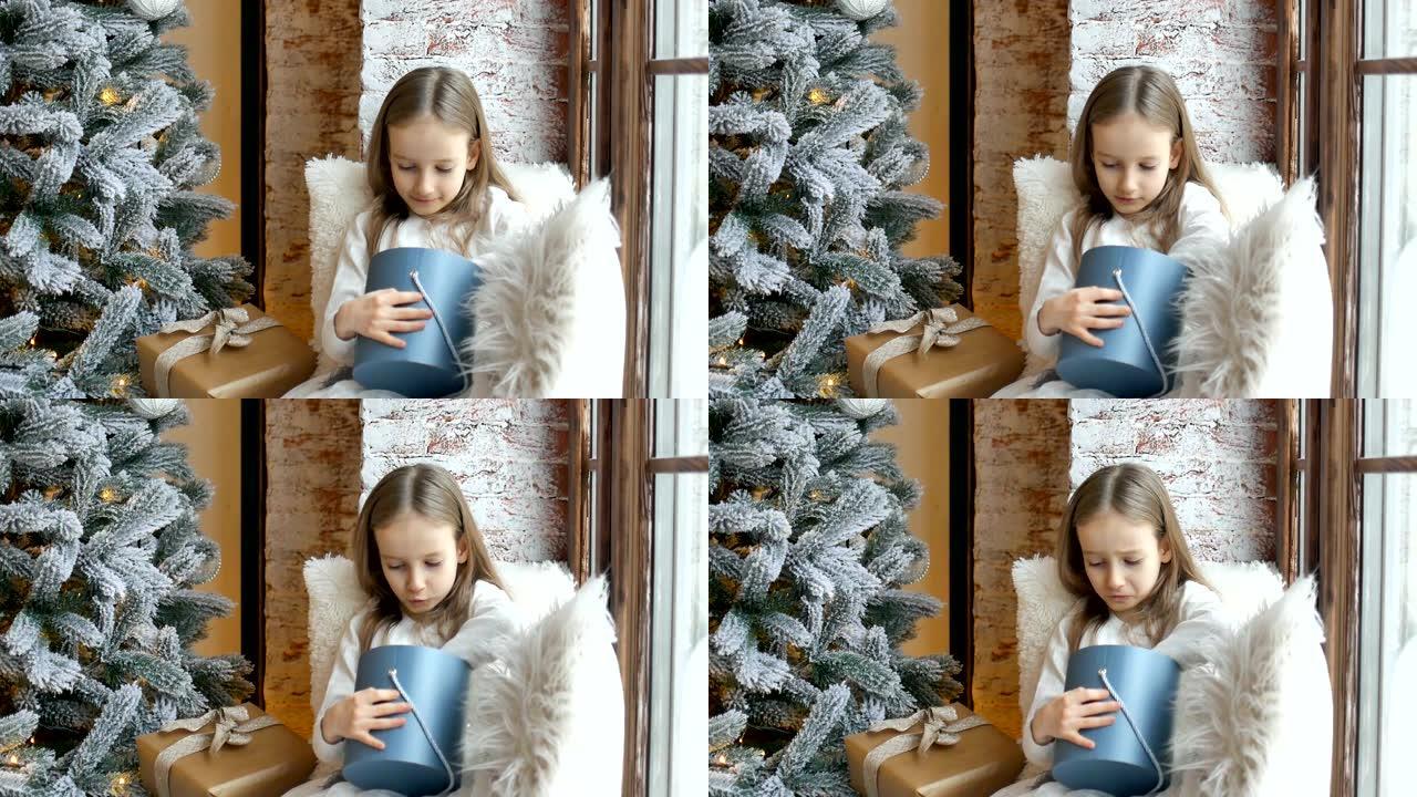 可爱的金发女孩正在打开深蓝色礼品盒，她坐在圣诞树附近，童年快乐和圣诞庆祝概念