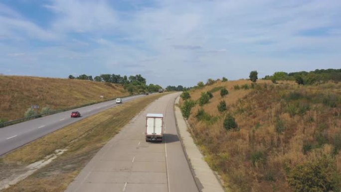 在高速公路上行驶并运输货物的卡车与货运拖车的空中射击。夏季通过乡村高速公路的大型送货卡车的视图。农村