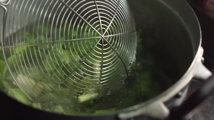 有人在开水的锅中使用滤网筛子和choy。中国蔬菜。慢动作