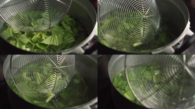 有人在开水的锅中使用滤网筛子和choy。中国蔬菜。慢动作