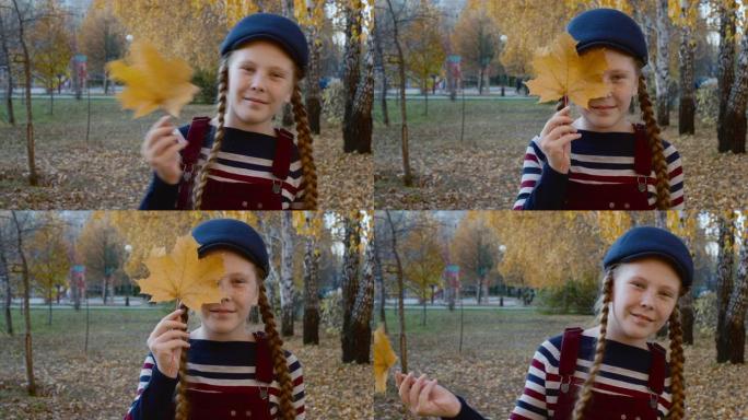 快乐的少女手握黄色枫叶靠近脸。秋天树叶公园的肖像顽皮女孩。面对雀斑的红发女孩。