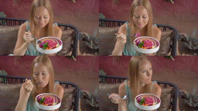 年轻女子坐在美丽的咖啡馆里，在碗里享受五颜六色的格兰诺拉麦片冰沙。健康饮食理念。慢动作镜头