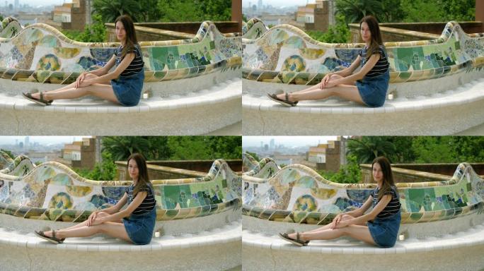 公园奎尔的主露台。一个快乐的年轻女子坐在瓷砖蛇形长椅上。巴塞罗那。西班牙。4K