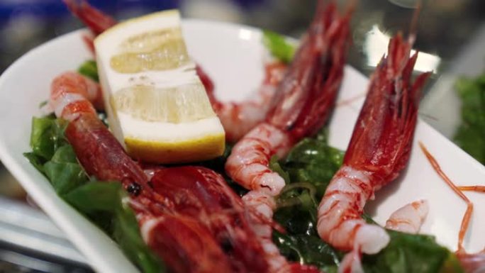 新鲜美味的皇家大虾躺在白色盘子里，柠檬和香草。鱼市场柜台上的异国情调的地中海虾，餐厅的豪华海鲜