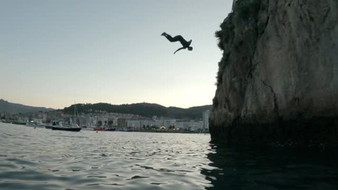身穿潜水服的小男孩在日落时从悬崖上跳入水中翻筋斗