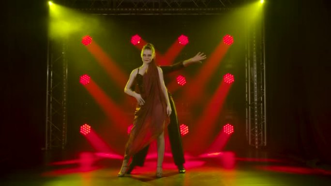 一对浪漫的舞厅舞者在演播室里，在红色聚光灯的背景下跳舞。慢动作