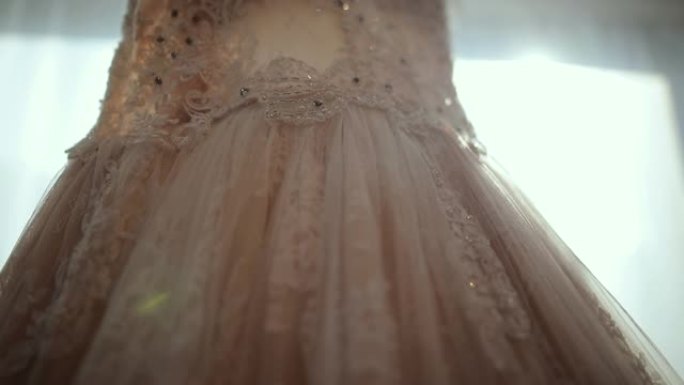 挂在窗户上的豪华现代婚纱。时尚柔和粉色婚纱，带蕾丝花卉细节