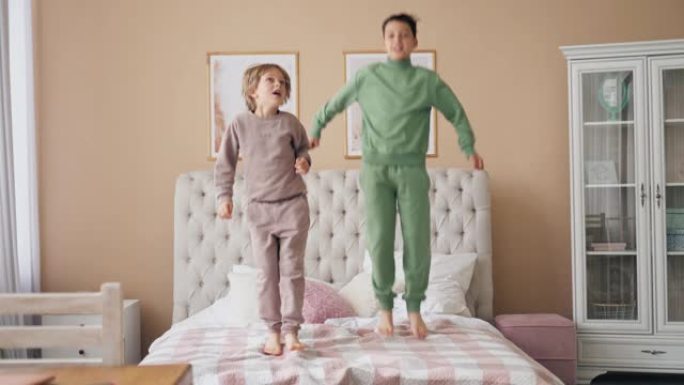 两个白人男孩在床上跳起来，开心地笑着和可爱的孩子儿子在卧室里玩有趣的活跃游戏。