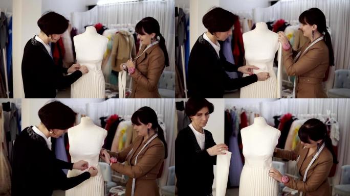 两位专业裁缝，设计师在工作室的模特上与新模特裁缝白色连衣裙一起工作。固定袖子并固定裙子。时尚和剪裁概