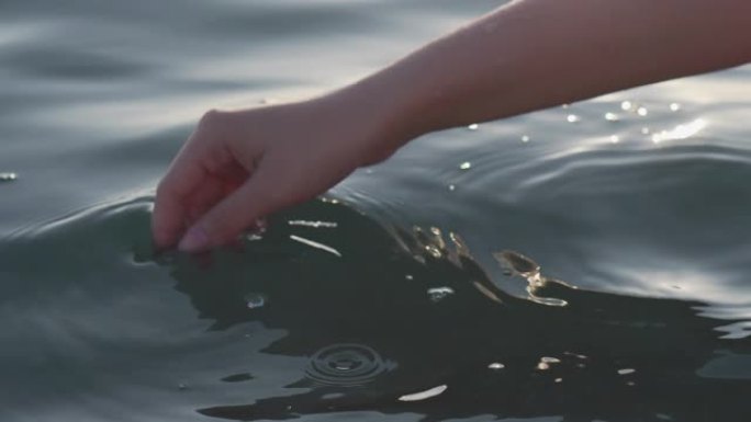 女性的手在夕阳的刺眼中嬉戏而轻柔地触摸海面，特写，