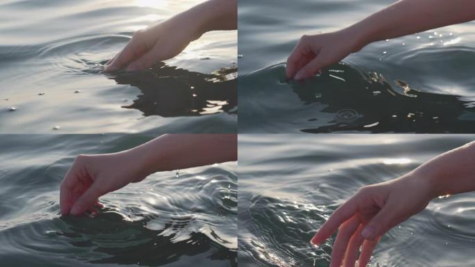 女性的手在夕阳的刺眼中嬉戏而轻柔地触摸海面，特写，