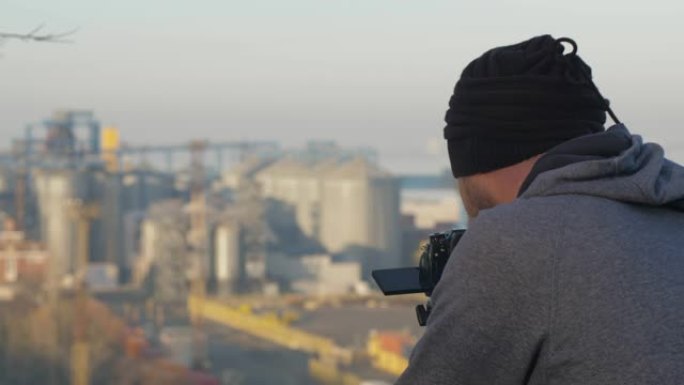 专业摄影师或摄像师用三脚架从山上移走海港。留胡子的摄影师在拍照。电影4k视频