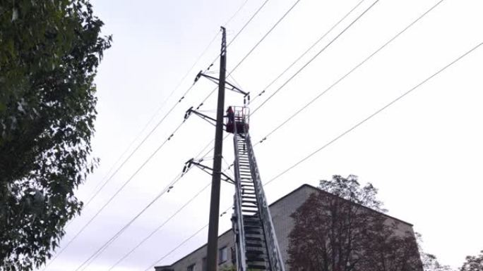 电工修理一排高压电线。可伸缩梯子和工人站立的摇篮的底视图。树木，天空和建筑物在背景中可见