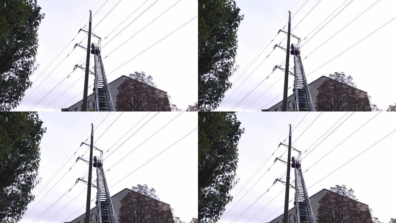 电工修理一排高压电线。可伸缩梯子和工人站立的摇篮的底视图。树木，天空和建筑物在背景中可见
